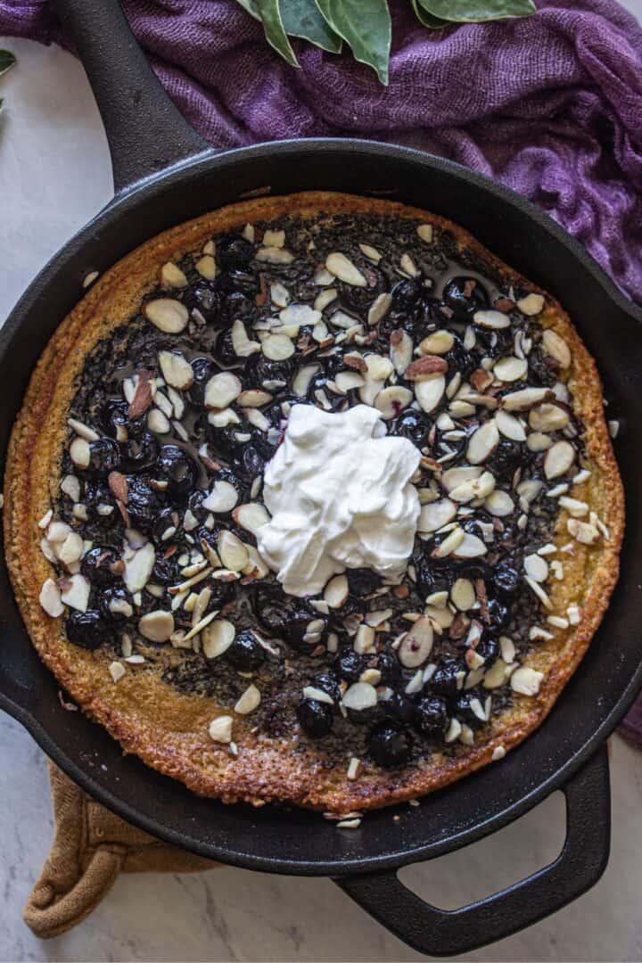a cast iron skillet with a gluten free oven baked pancake (dutch baby) with blueberry sauce, sliced almonds and greek yogurt on top