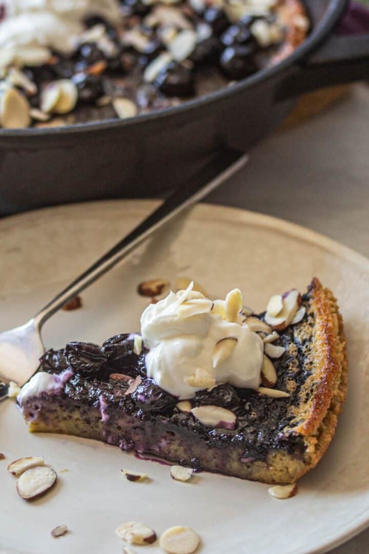 a slice of gluten fee oven baked pancake (dutch baby) with blueberry sauce, sliced almonds and greek yogurt on top