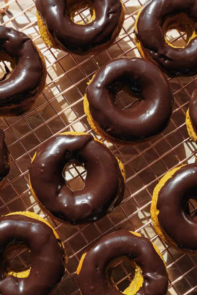 a cooling rack of gluten free baked pumpkin donuts with gluten free chocolate glaze