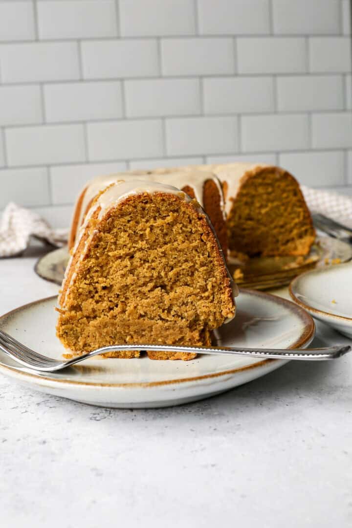 a slice of gluten free pumpkin bundt cake on a plate in front of the entire bundt cake on a platter