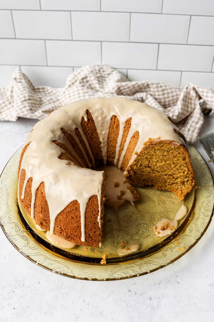 gluten free pumpkin bundt cake on a yellow round glass platter next to a tan and white gingham kitchen towel