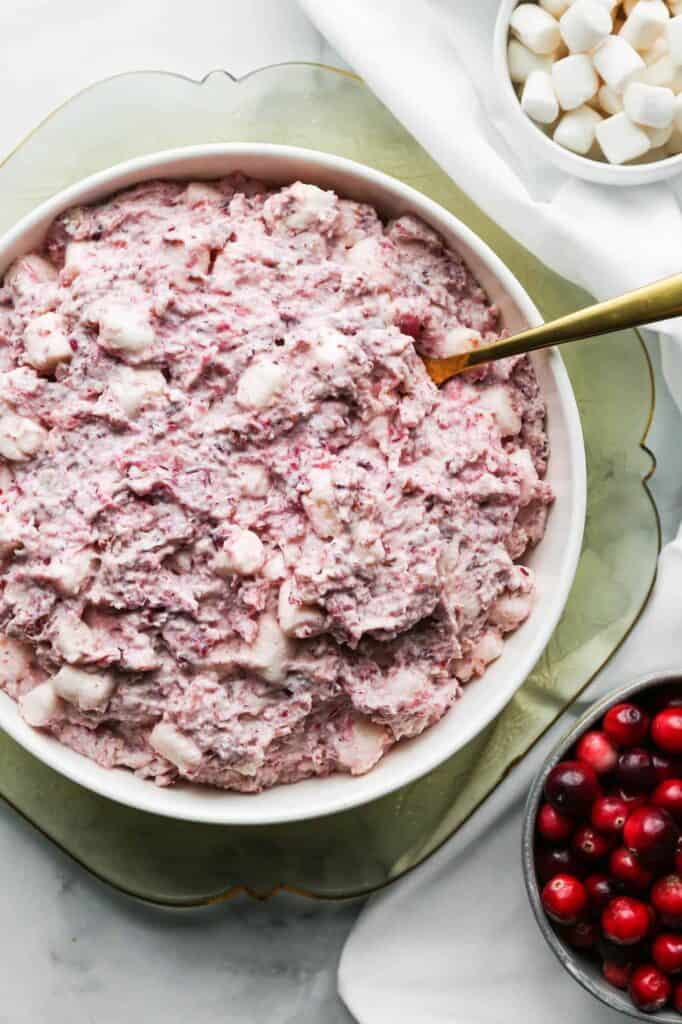 a serving bowl of cranberry fluff salad with small bowls of marshmallows and fresh cranberries beside it
