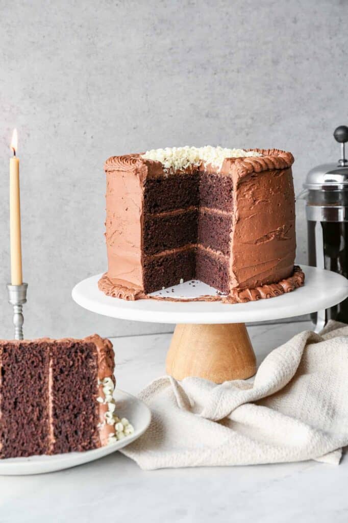 a gluten free chocolate mayonnaise cake on a cake stand with a slice of cake on a plate and a pot of coffee