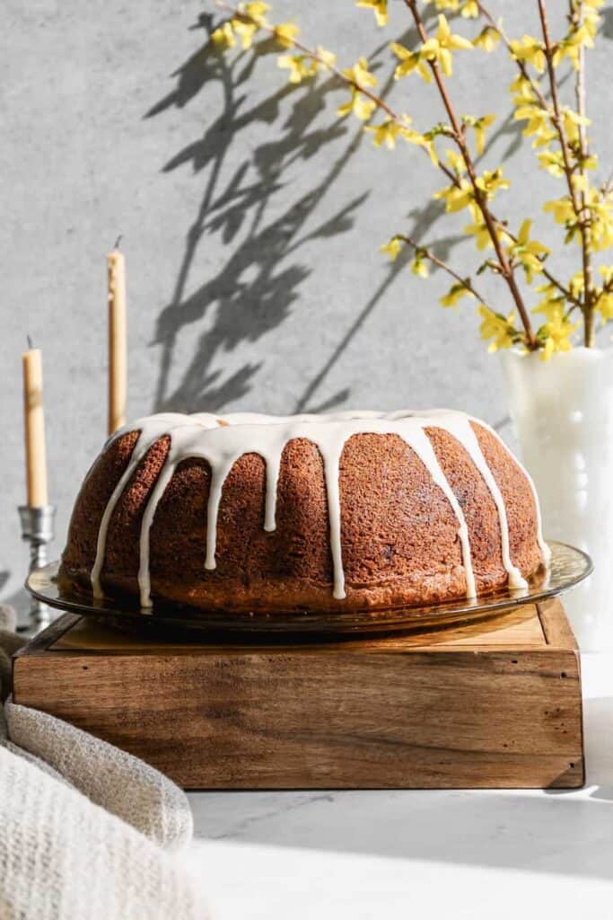 a gluten free hummingbird bundt cake with glaze on top sitting on an antique yellow plate and a wooden box