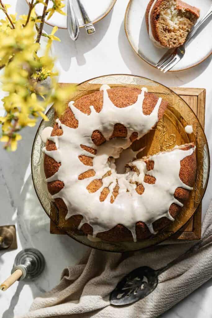 a gluten free hummingbird bundt cake on a antique yellow platter with yellow forsythia blooms next to the cake