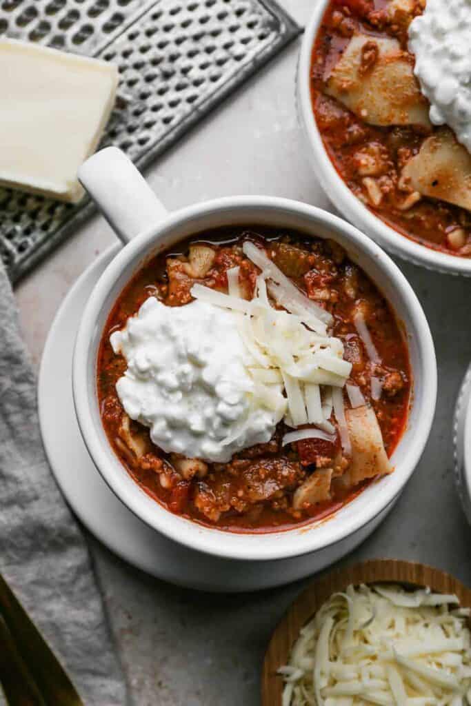 a large white mug of gluten free slow cooker lasagna soup with cottage cheese and shredded mozzarella cheese on top