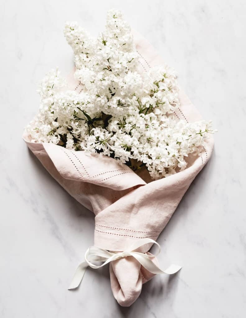 a marble background with one of my favorite things, white lilac blooms wrapped in a light pink linen napkin and tide with white ribbon