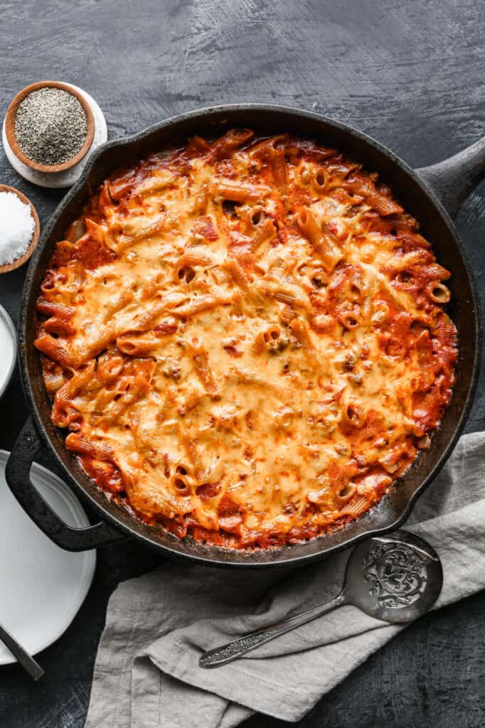 a cast iron skillet of gluten free taco pasta bake with a pinch bowl of salt and pepper and a bowl of sour cream