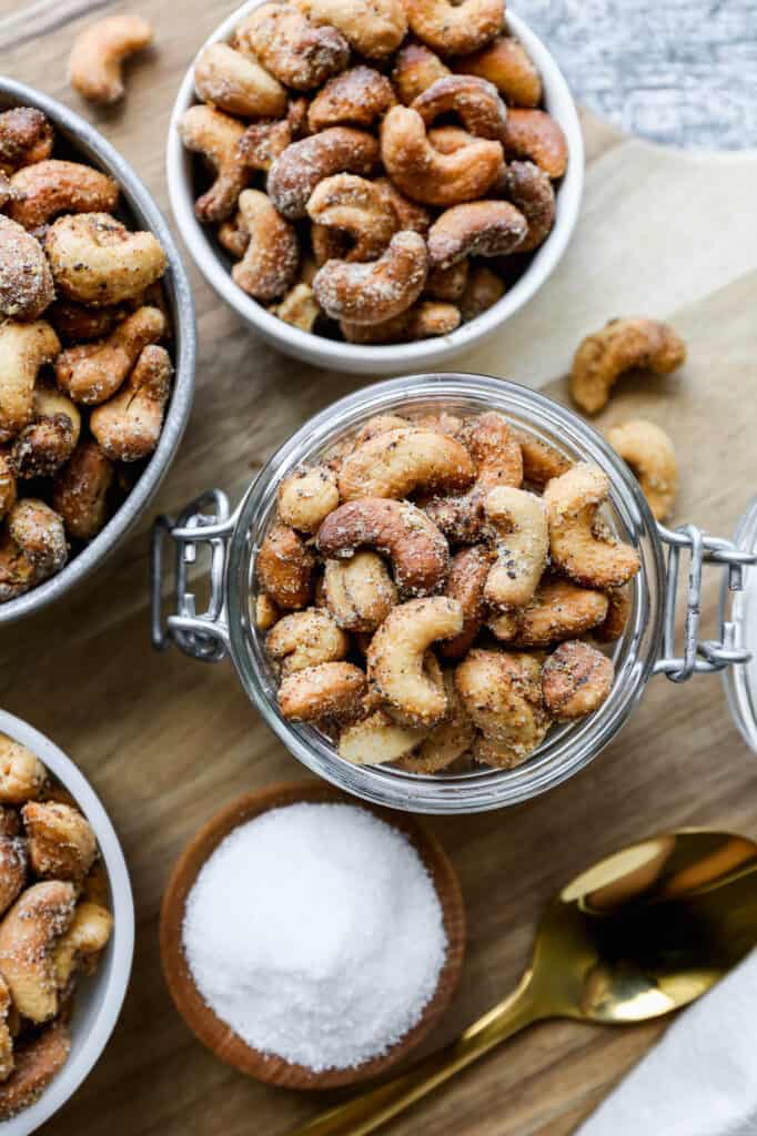 small bowls of air fryer salt and pepper roasted cashews on a round wooden cutting board