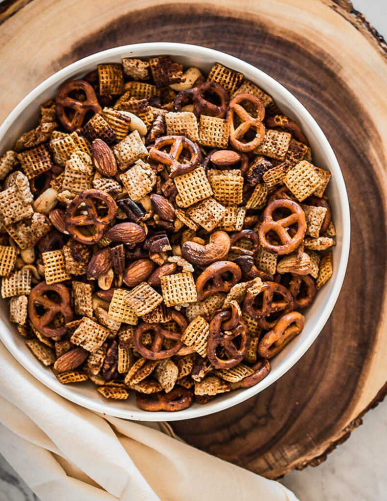 a white bowl of gluten free air fryer chex mix on a round wooden tray