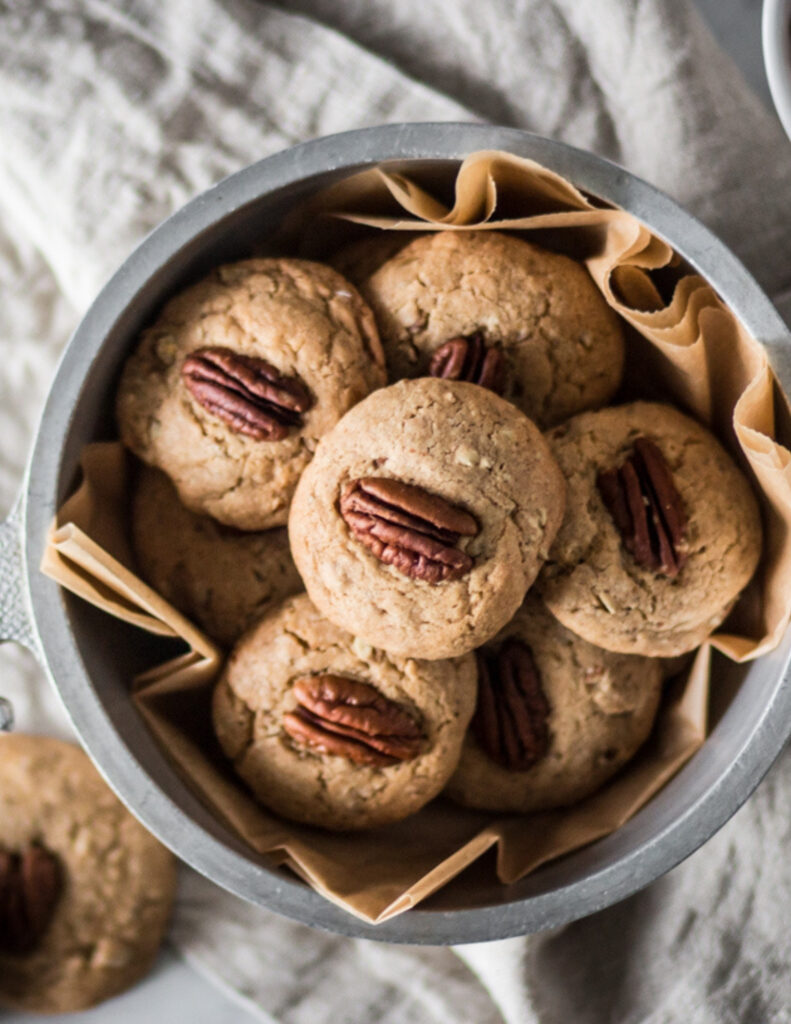 a silver bowl of gluten free butter pecan cookies next to a bowl of pecans on a marble surface