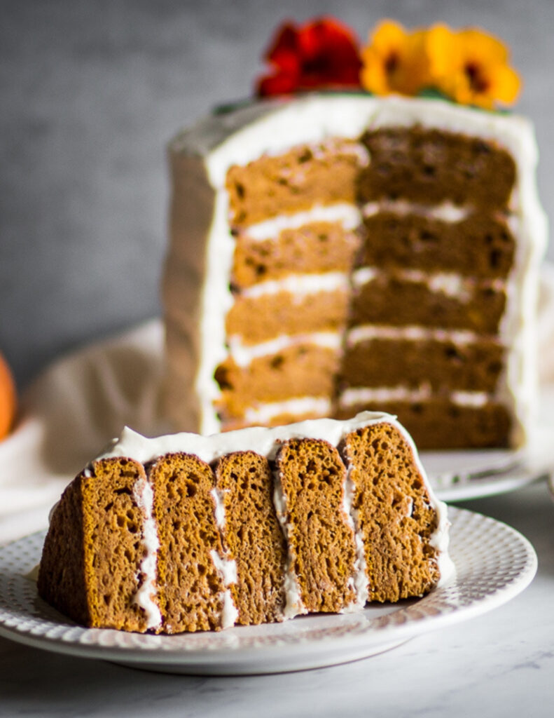 a gluten free pumpkin cake with cream cheese frosting on a plate with a slice and an orange pumpkin next to it