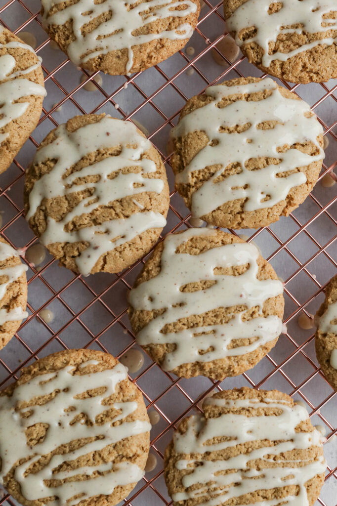 a copper cooling rack of gluten free eggnog cookies with eggnog icing drizzled overtop