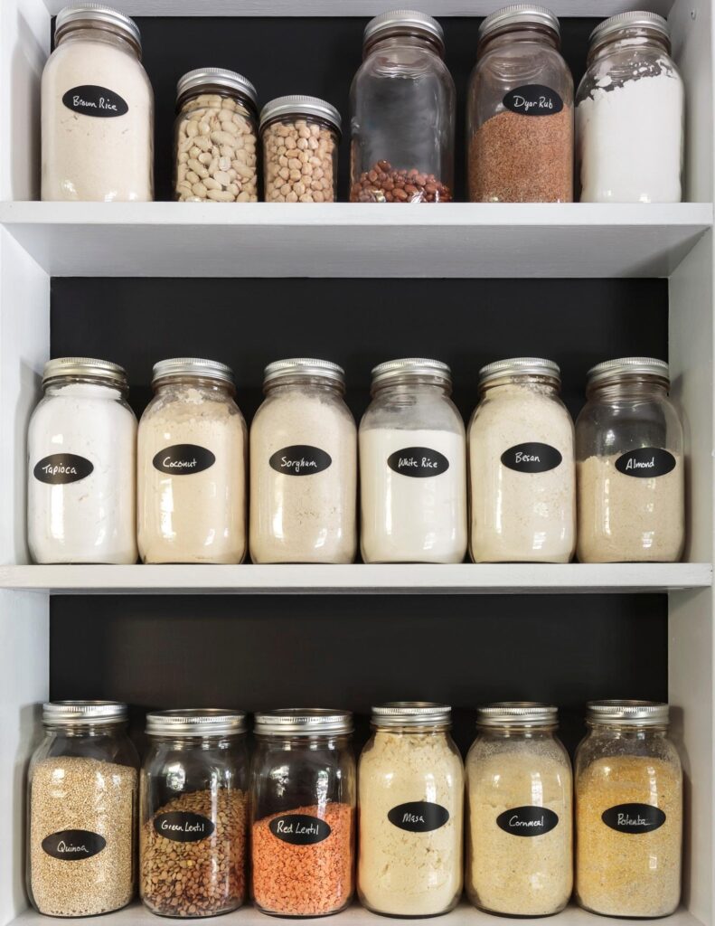 white shelves with jars  that have black labels on them saying what is in them.