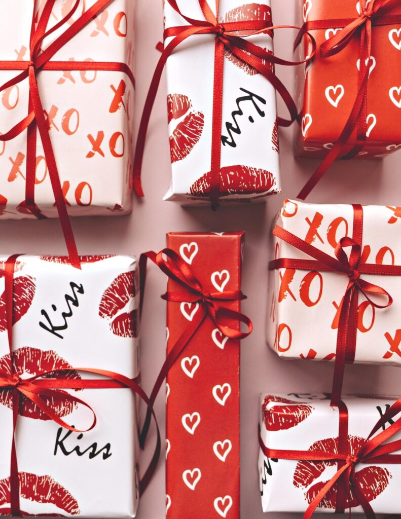 Presents wrapped in valentine's day paper with hearts, lips, kisses and xo with red ribbons tied around them.