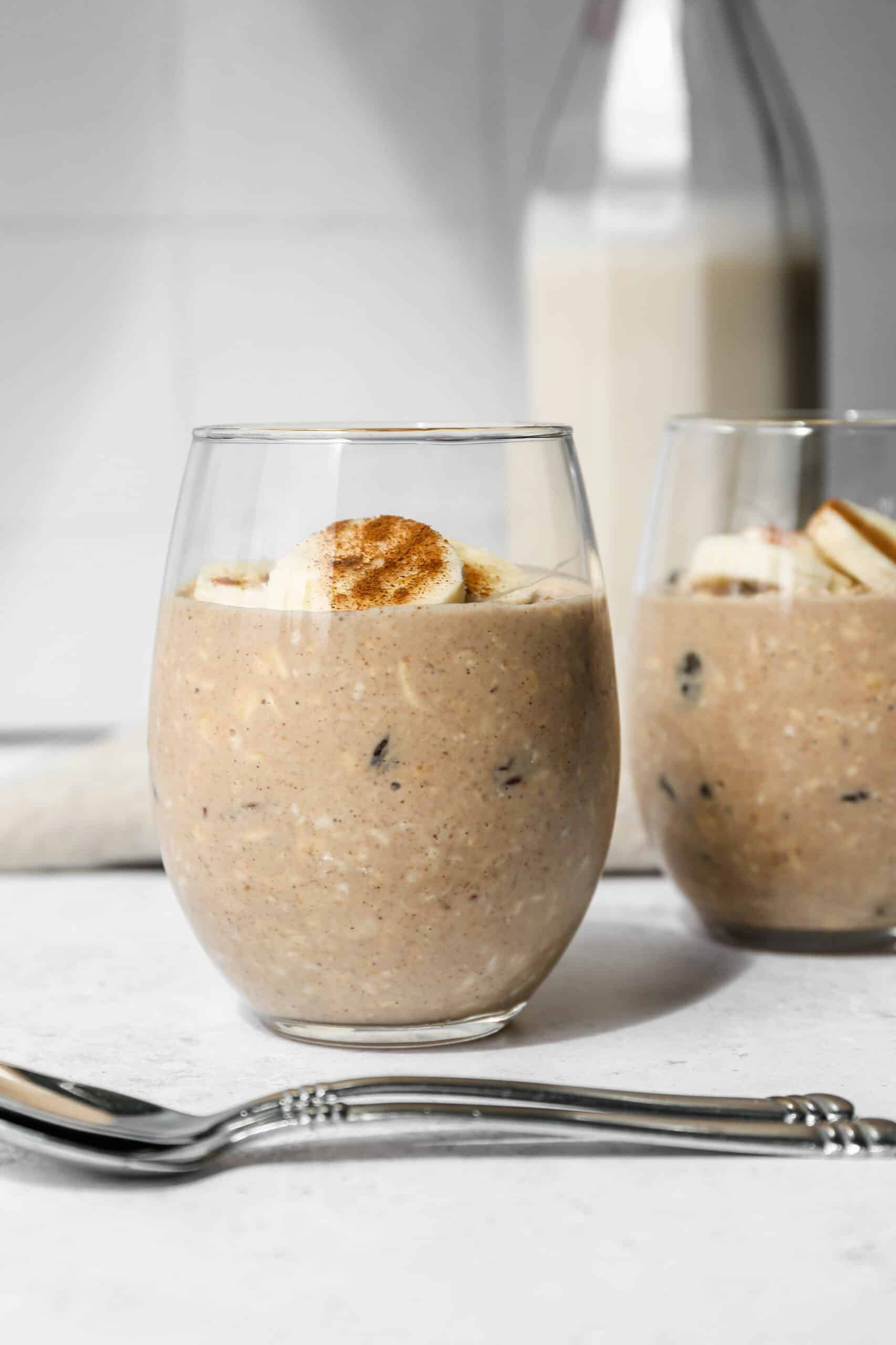 a stemless wine glass of gluten free oatmeal raisin overnight oats with banana slices and cinnamon sprinkled on top.