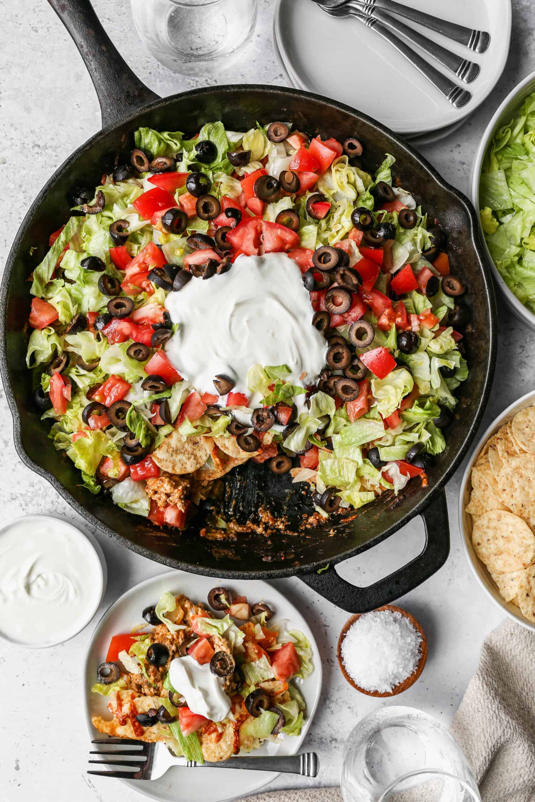a black cast iron skillet of gluten free walking taco casserole with a big dollop of sour cream on top.