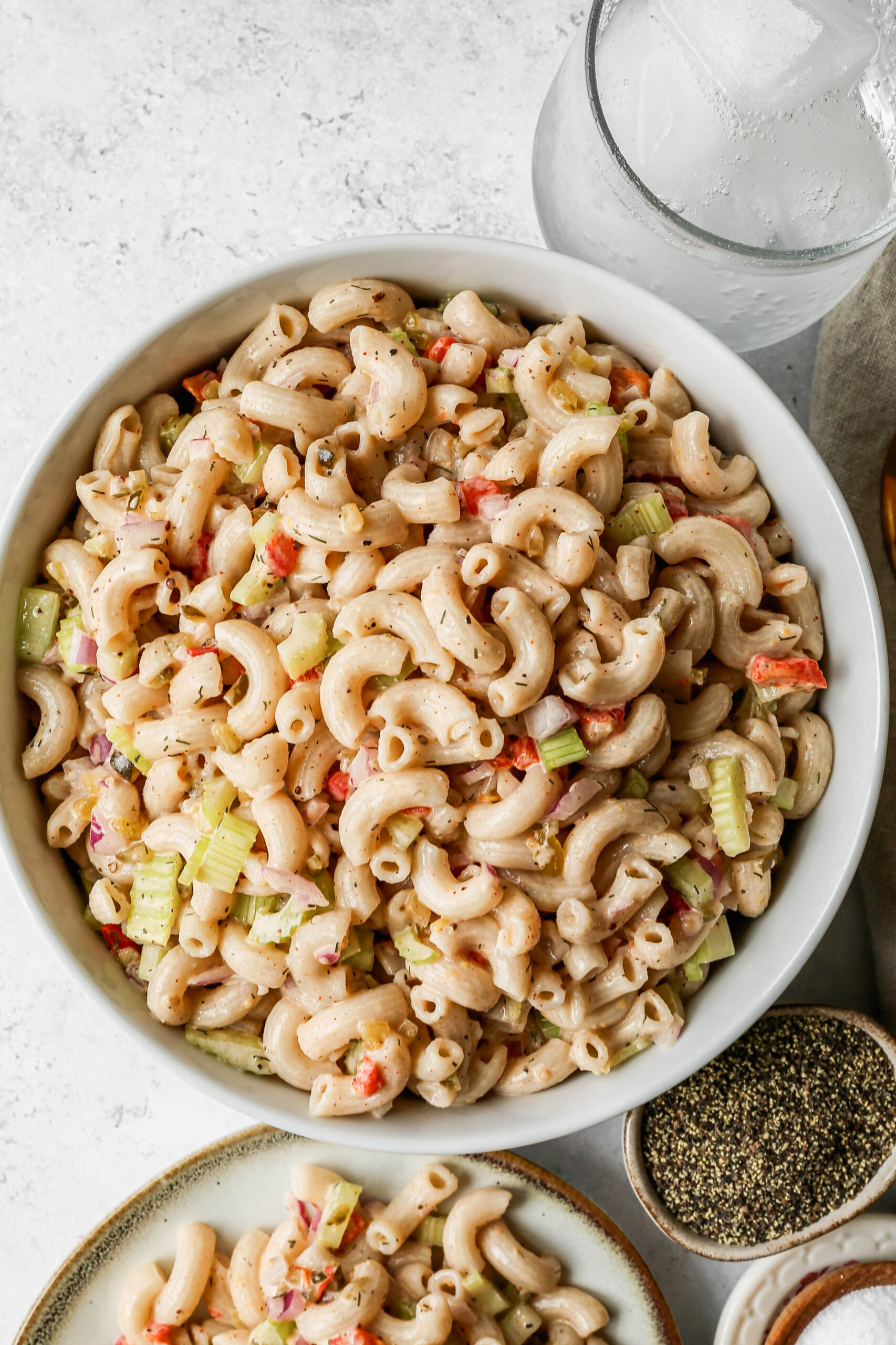 a large white bowl of easy gluten free macaroni salad next to a plate of cold salad.