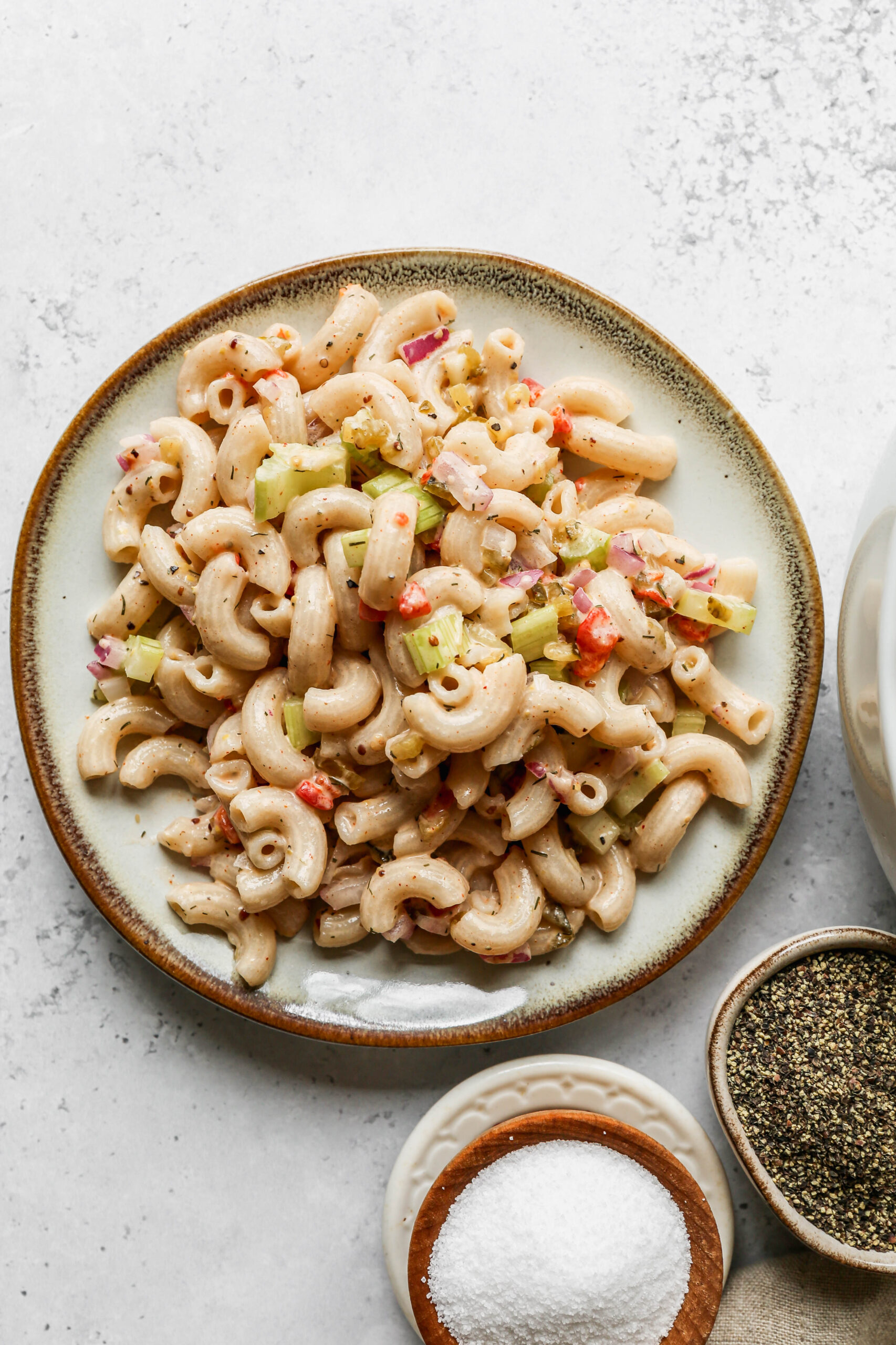 a plate of easy gluten free macaroni salad next to a small wooden bowl of salt.