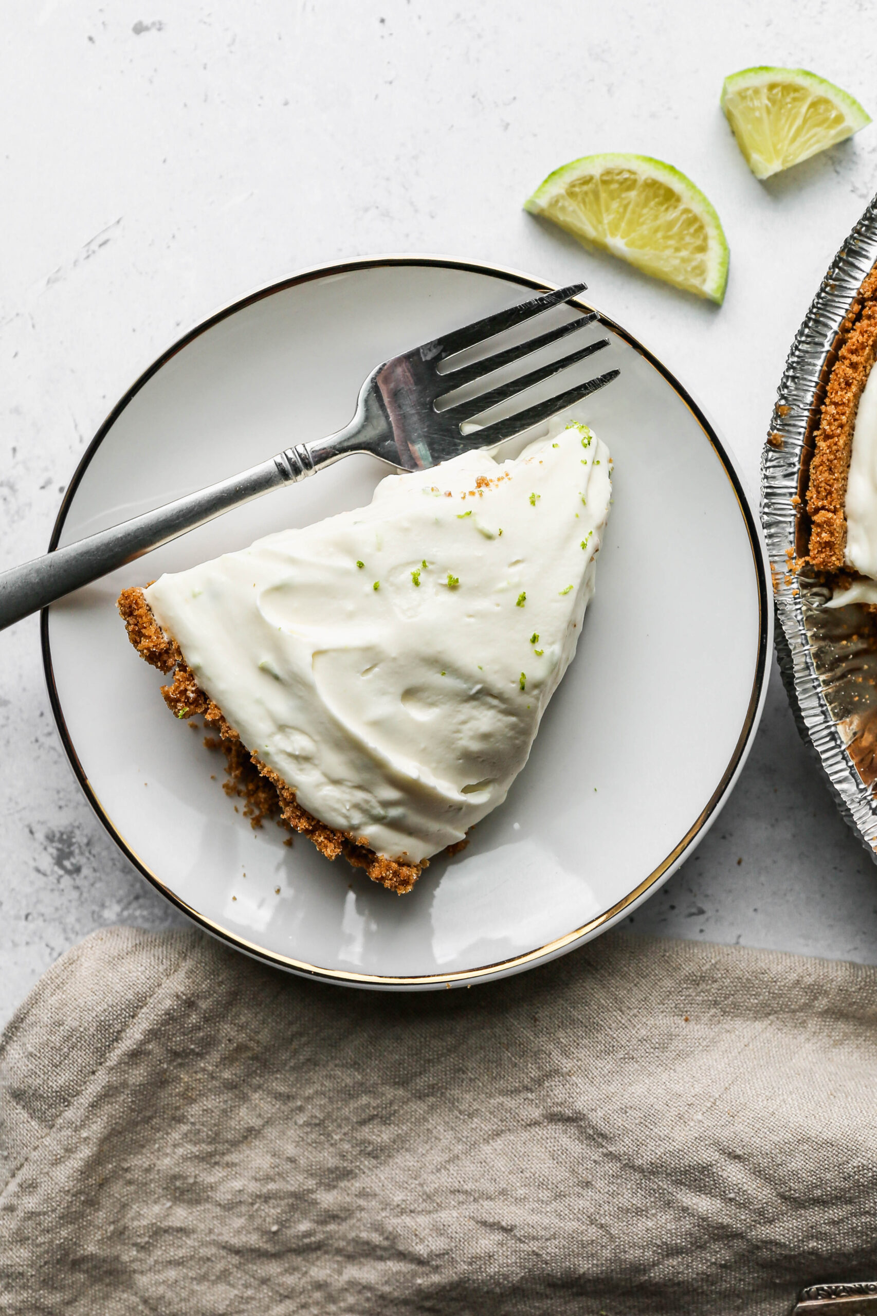 a slice of gluten free no bake key lime pie on a white plate next to a slices lime.
