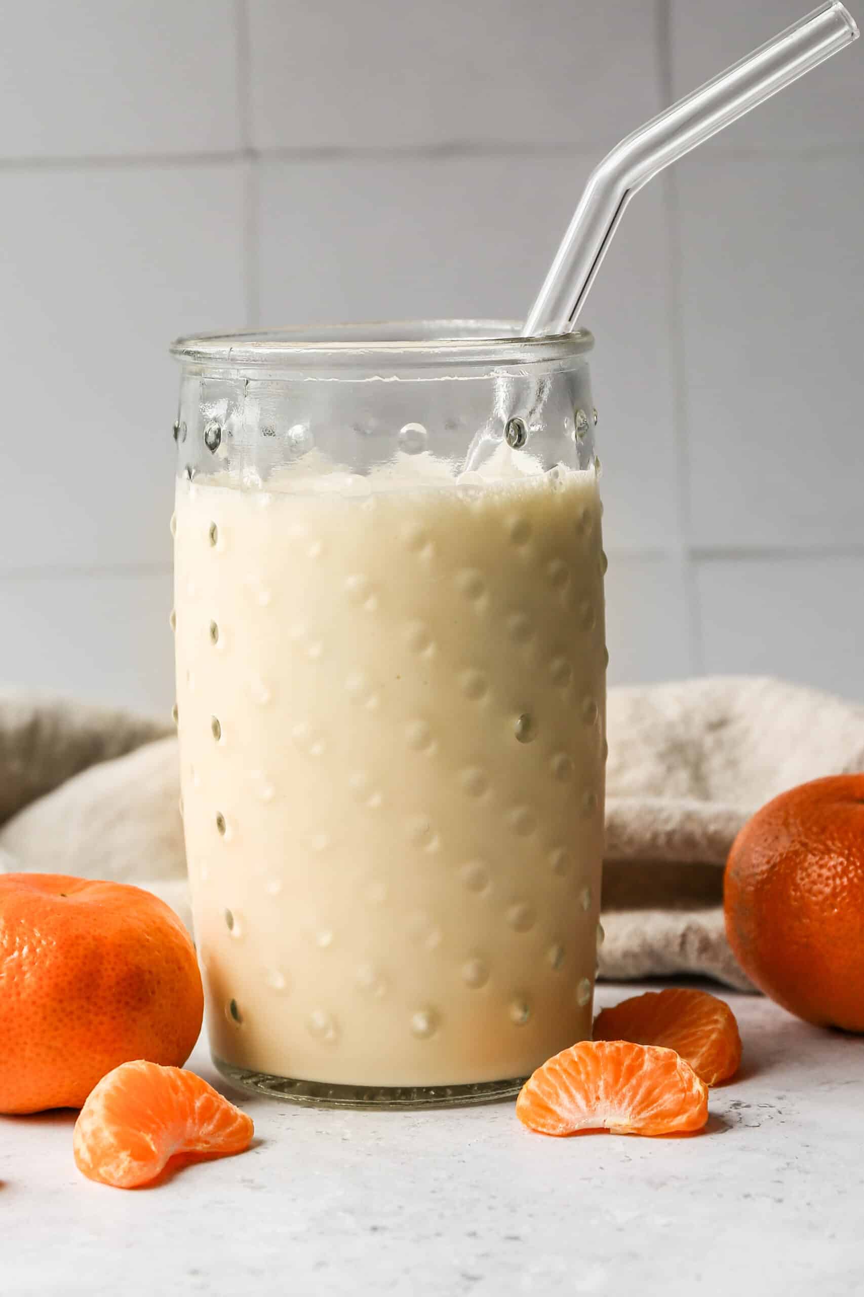 a clear glass of gluten free orange creamsicle smoothie with a glass straw.