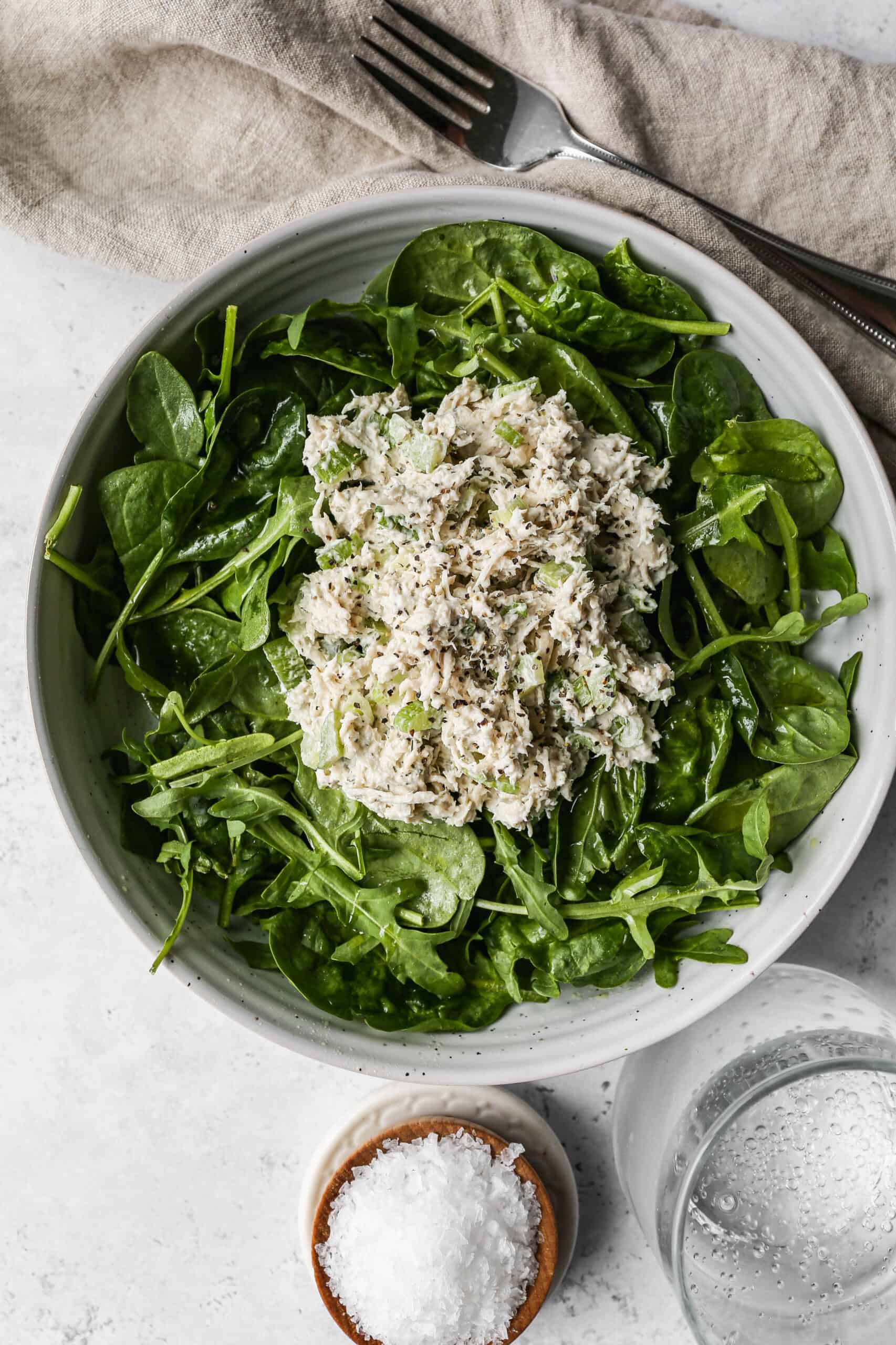 a white bowl of the best old fashioned chicken salad on top of baby spinach and arugula.