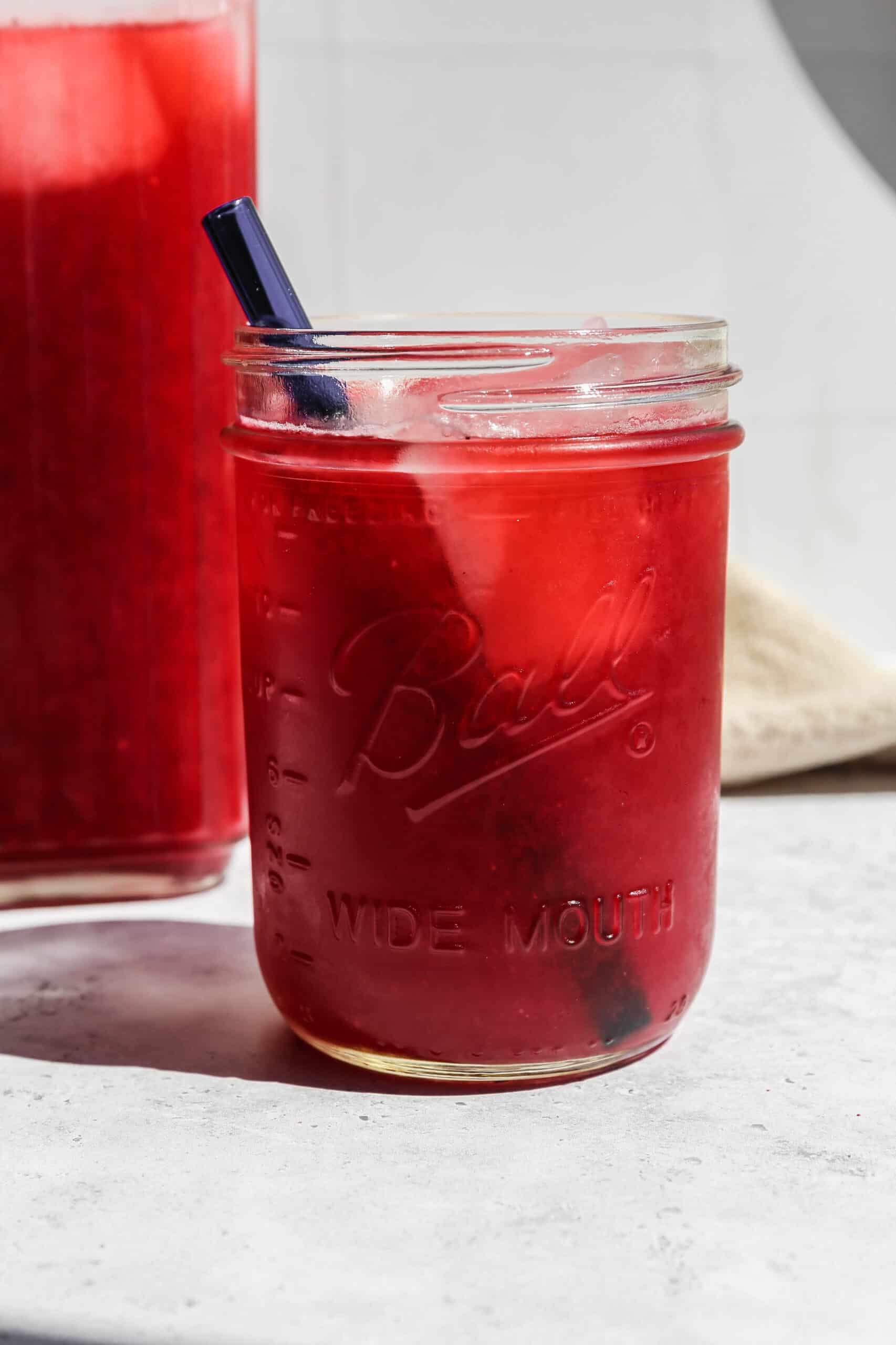 a wide mouth pint jar of homemade blackberry lemonade with a blue glass straw.