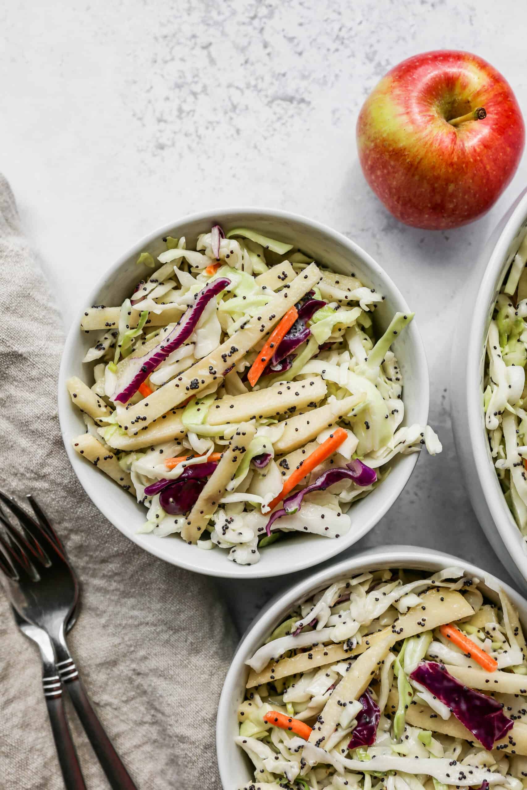 a small white bowl of easy apple slaw with poppyseed dressing next to a big white bowl of the salad.