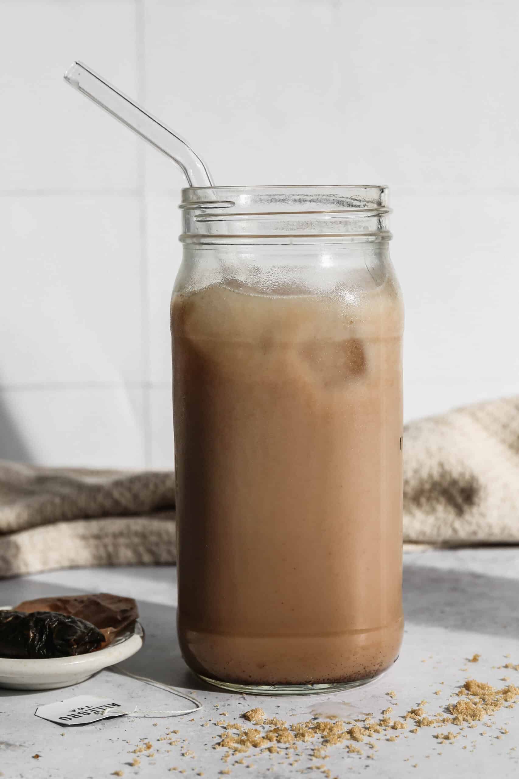 a glass jar of iced chair tea latte concentrate made into a drink using almond milk.