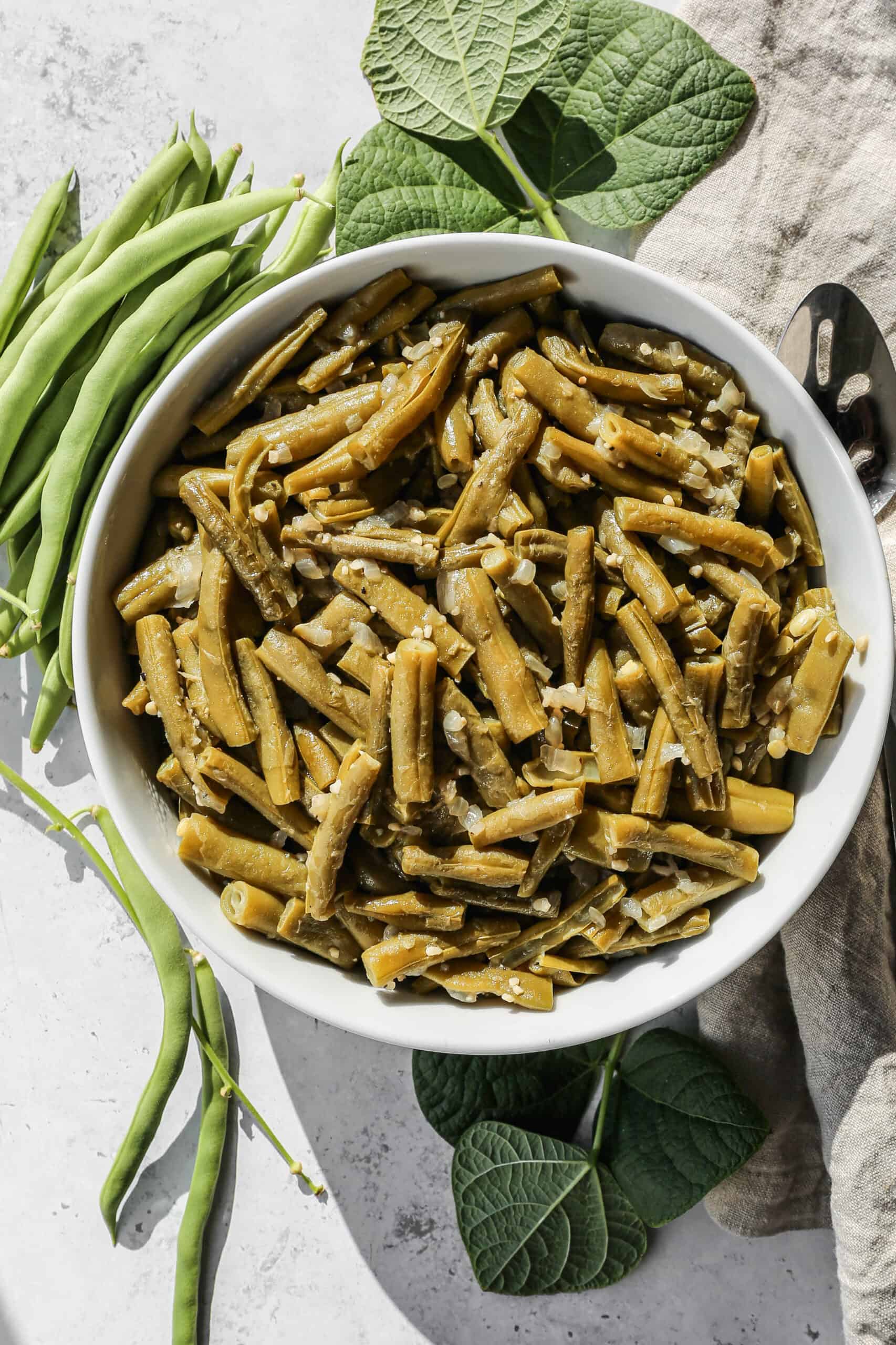 a white serving bowl of instant pot garlic ginger green beans next to fresh green beans.