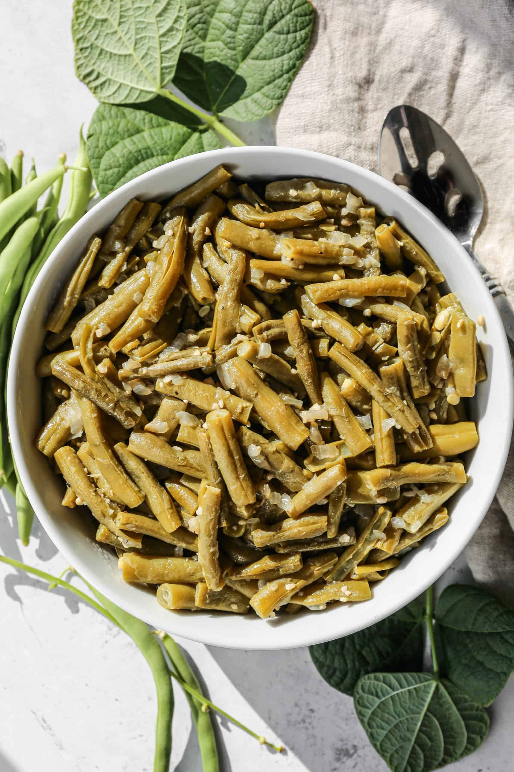 a white serving bowl of instant pot garlic ginger green beans next to fresh green beans.