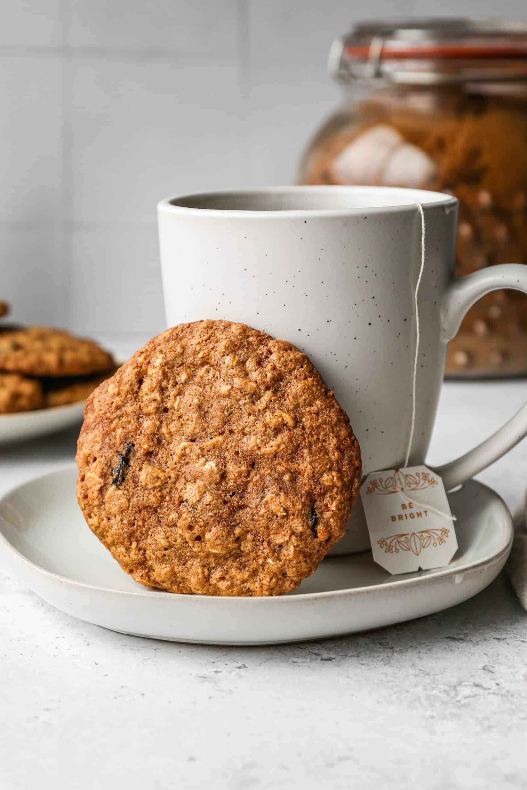 a white mug of tea with a gluten free oatmeal raisin cookie next to it.