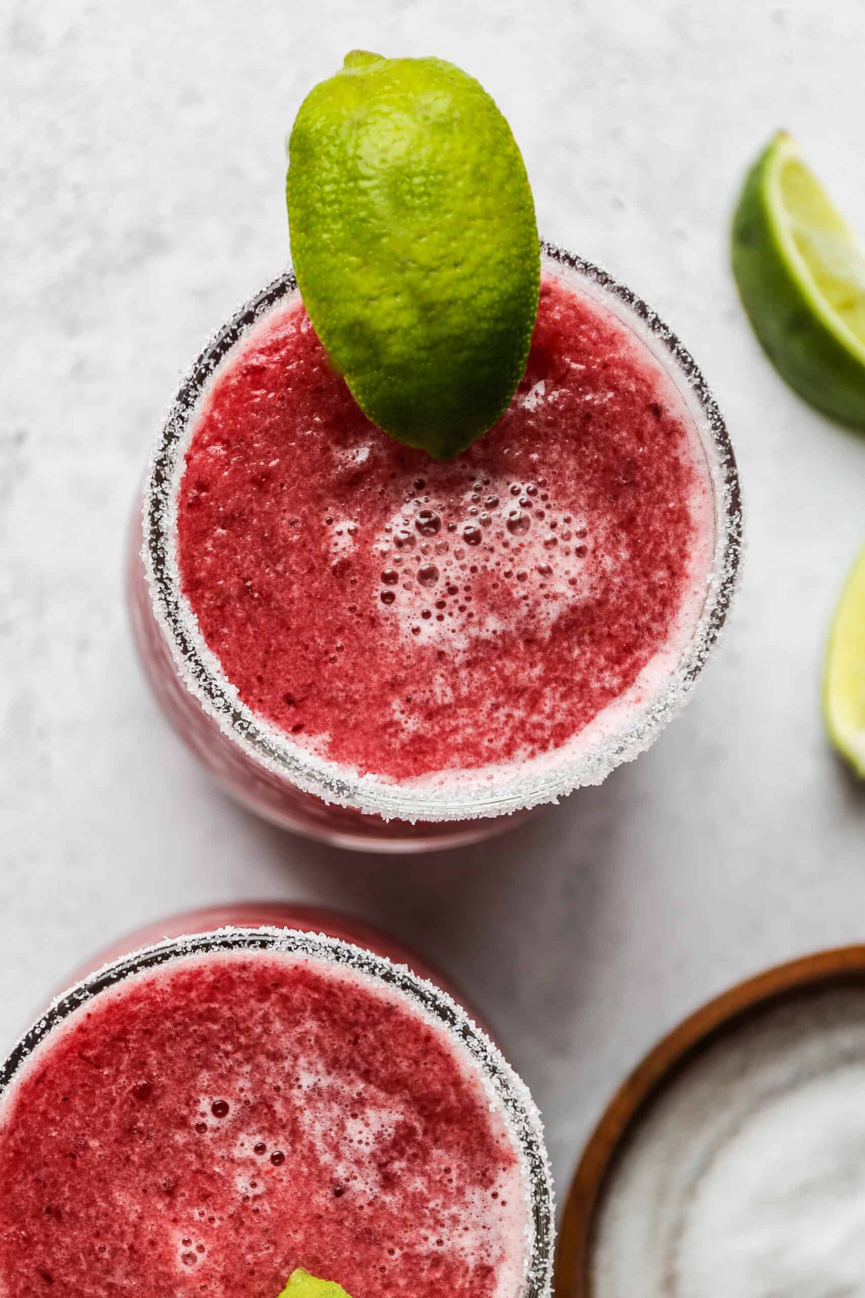 a glass of frozen cranberry margarita mocktail with salt on the rim and a lime wedge.