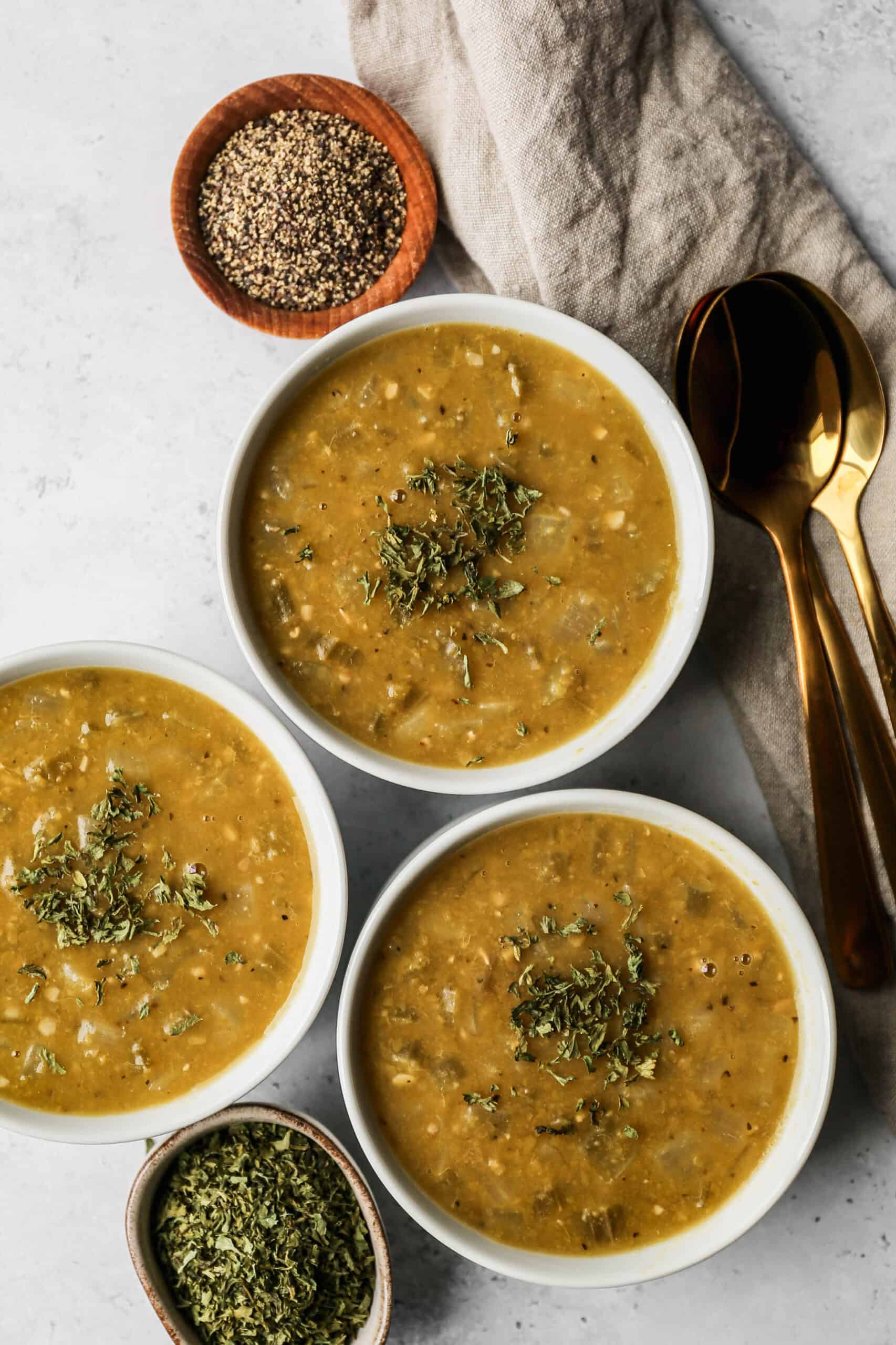 three white bowls of gluten free vegetarian instant pot split pea soup next to a small wooden bowl of pepper.