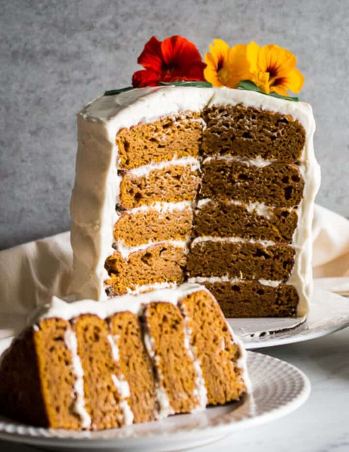 a layered gluten free pumpkin cake with cream cheese frosting between the layers and on the outside with a slice laying in front of it on a plate