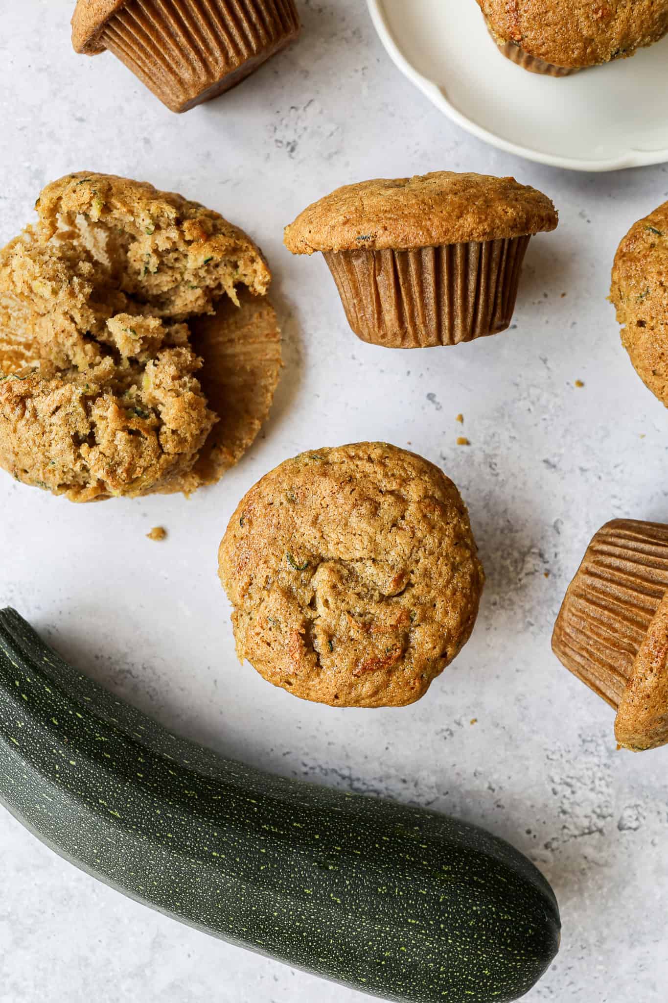 gluten free zucchini muffins sitting on the counter with one on a plate and one torn in half to show the center