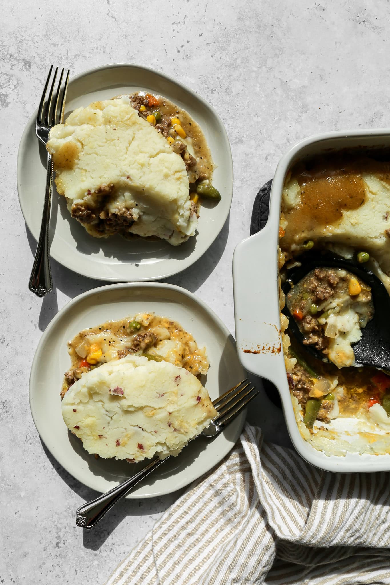 Two cream plates of gluten free easy ground beef shepherd's pie next to a cream 9x13 baking dish of the casserole
