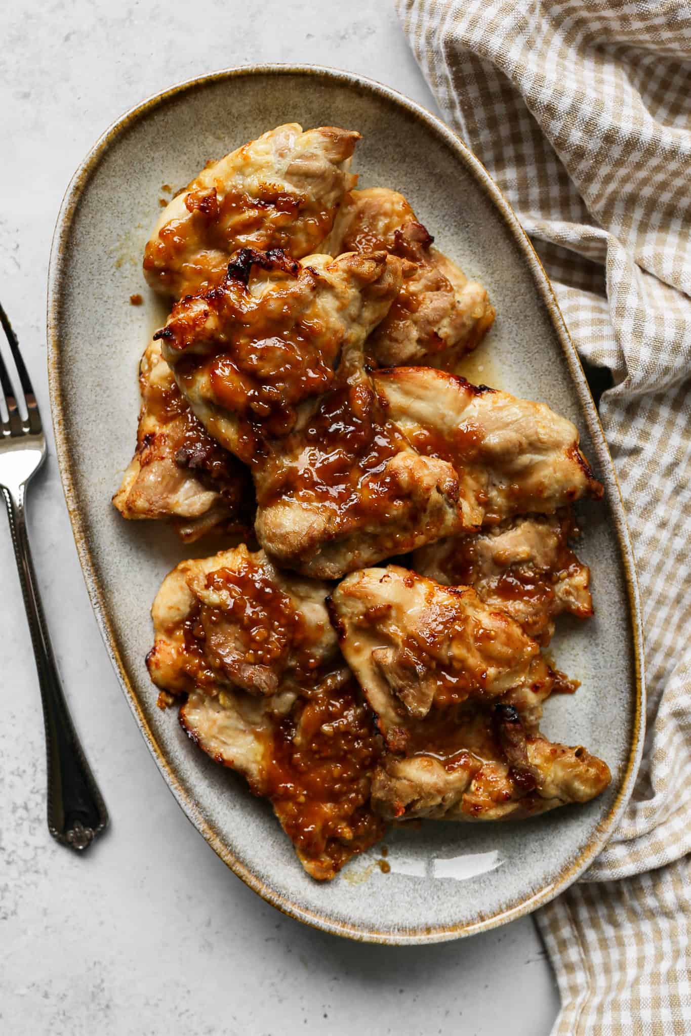 air fryer honey mustard chicken thighs on a platter next to a silver fork and a tan gingham kitchen towel