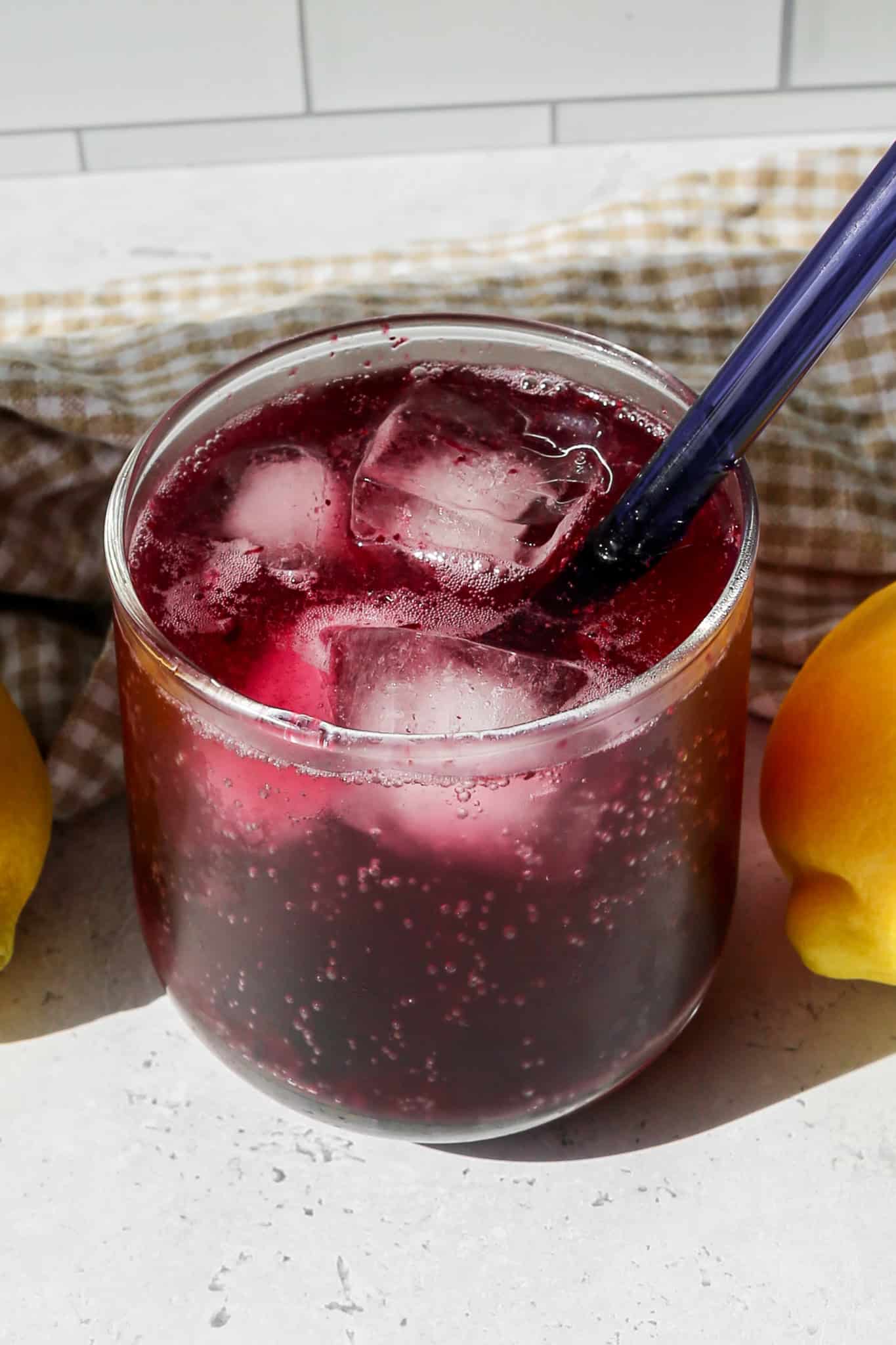 a short clear drinking glass of blueberry lemon sparkling mocktail over ice with a short blue straw
