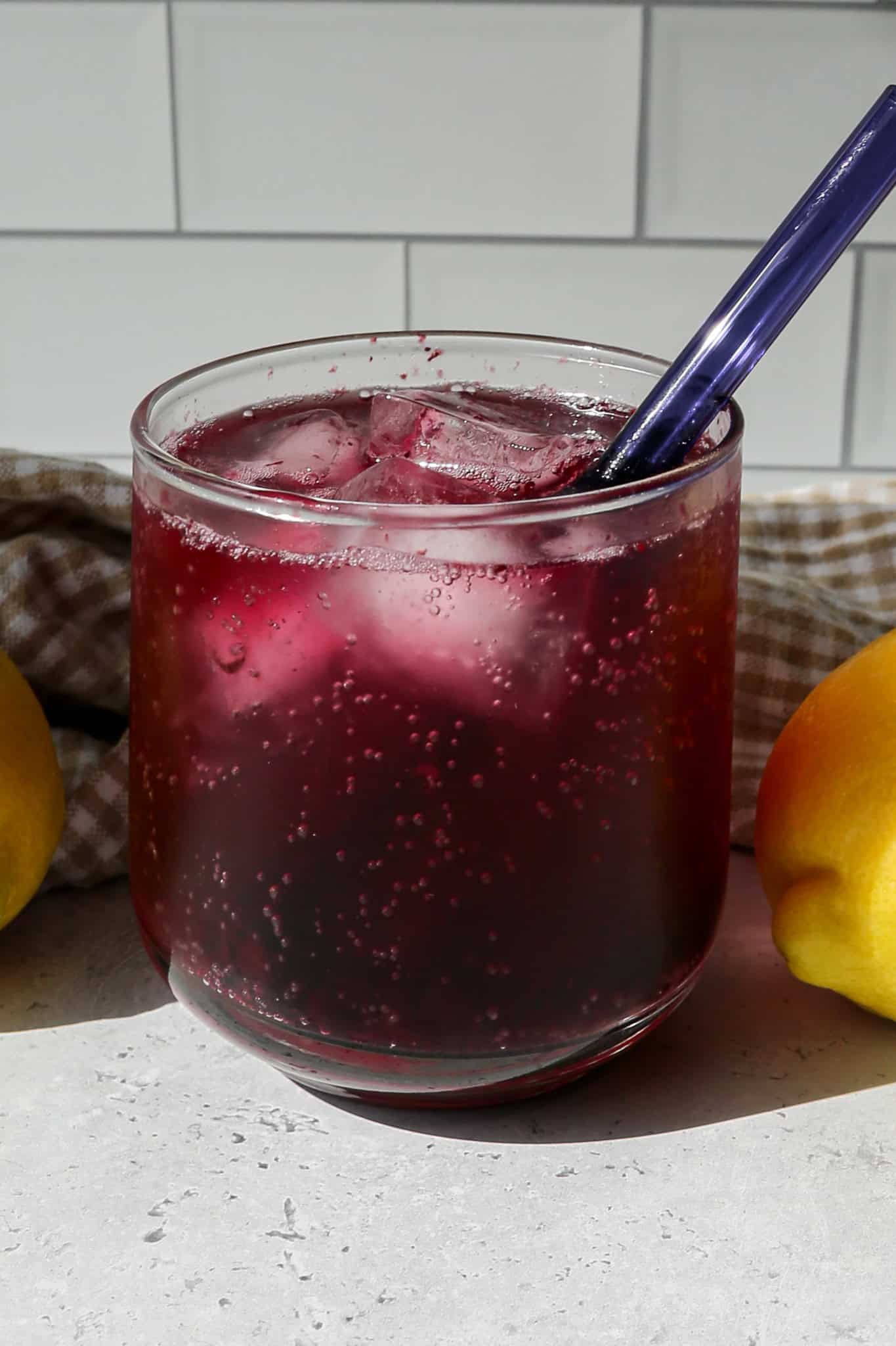 a short clear drinking glass of blueberry lemon sparkling mocktail over ice with a short blue straw