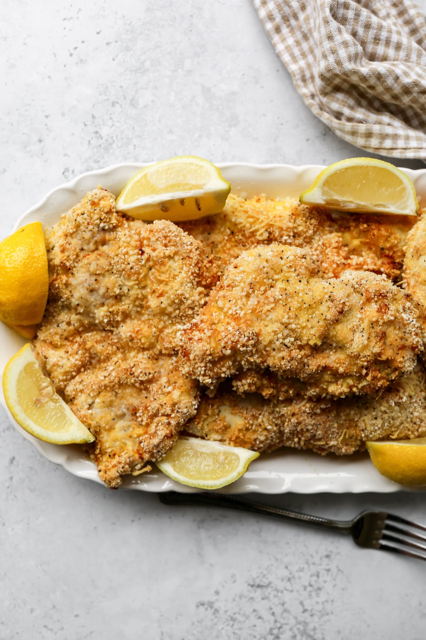 gluten free crispy air fryer chicken cutlets on a white platter next to a tan and white gingham kitchen towel