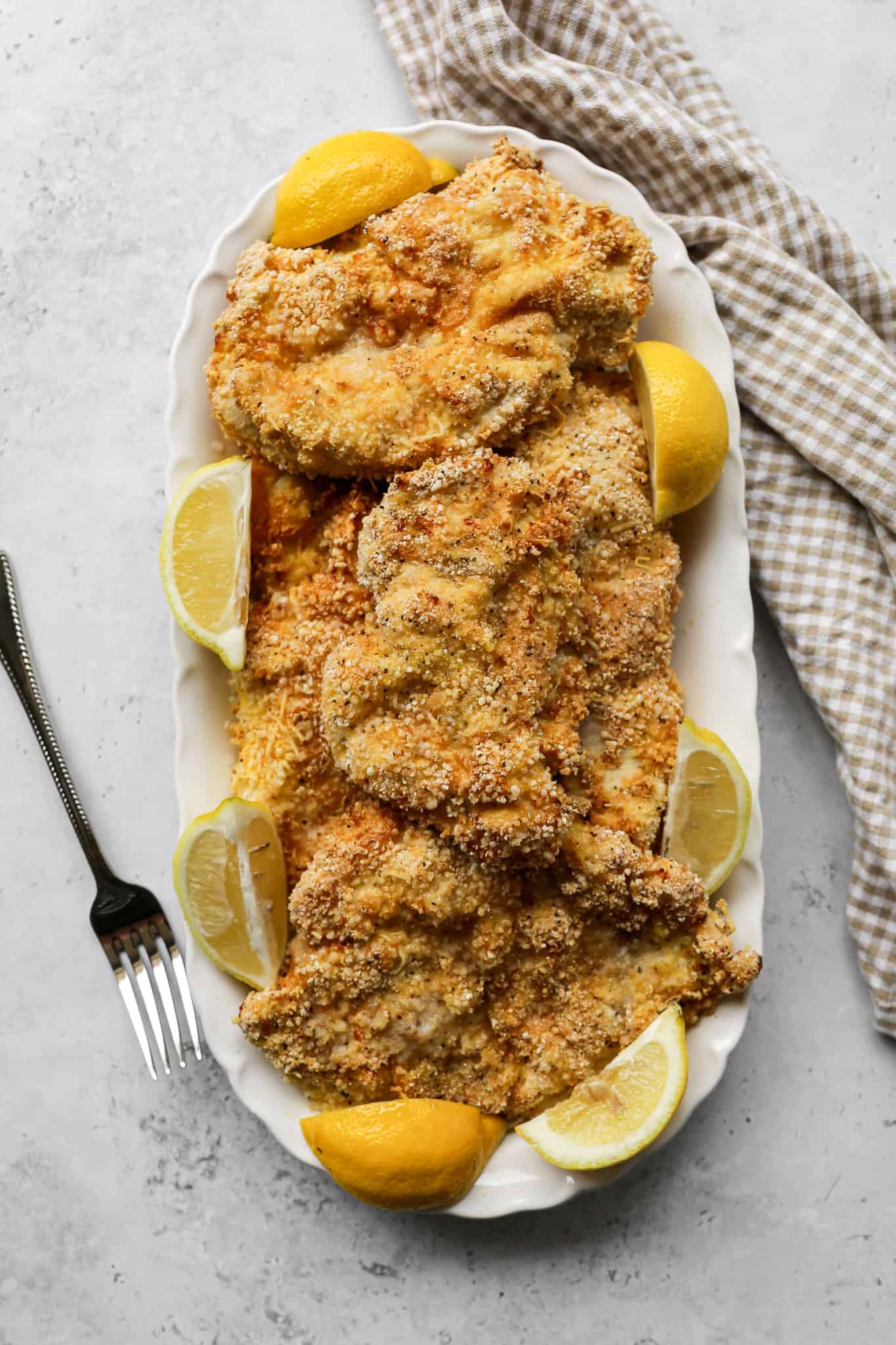 gluten free crispy air fryer chicken cutlets on a white platter next to a tan and white gingham kitchen towel