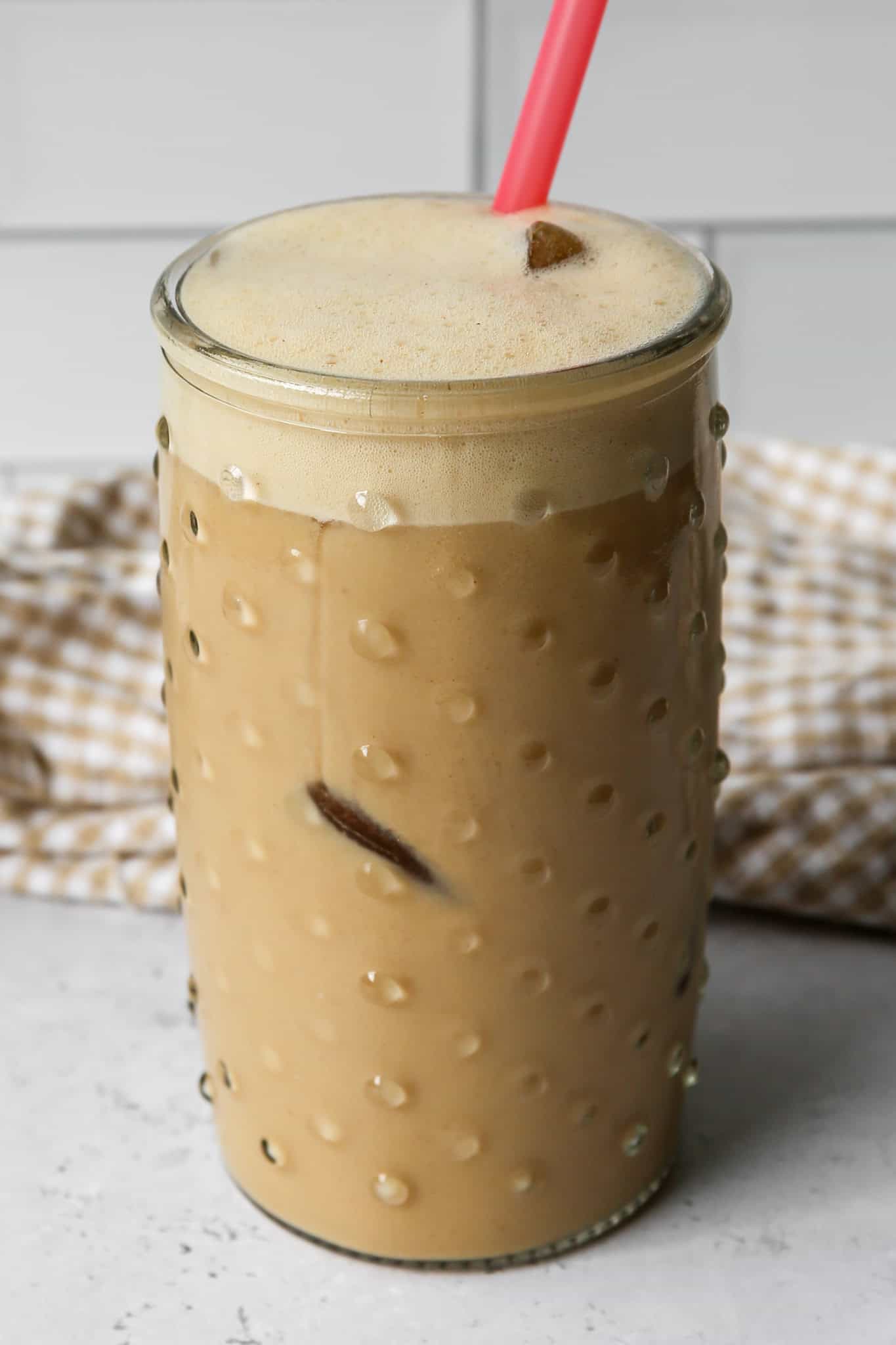 a clear hobnail drinking glass of high protein vanilla iced espresso over ice with a pink color change straw