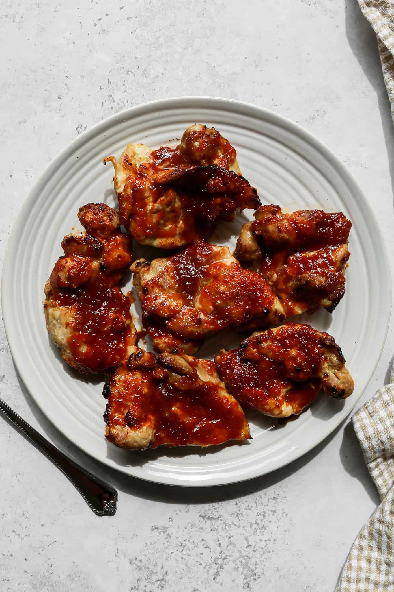 air fryer barbecue chicken thighs on a white plate next to a tan and white gingham kitchen towel