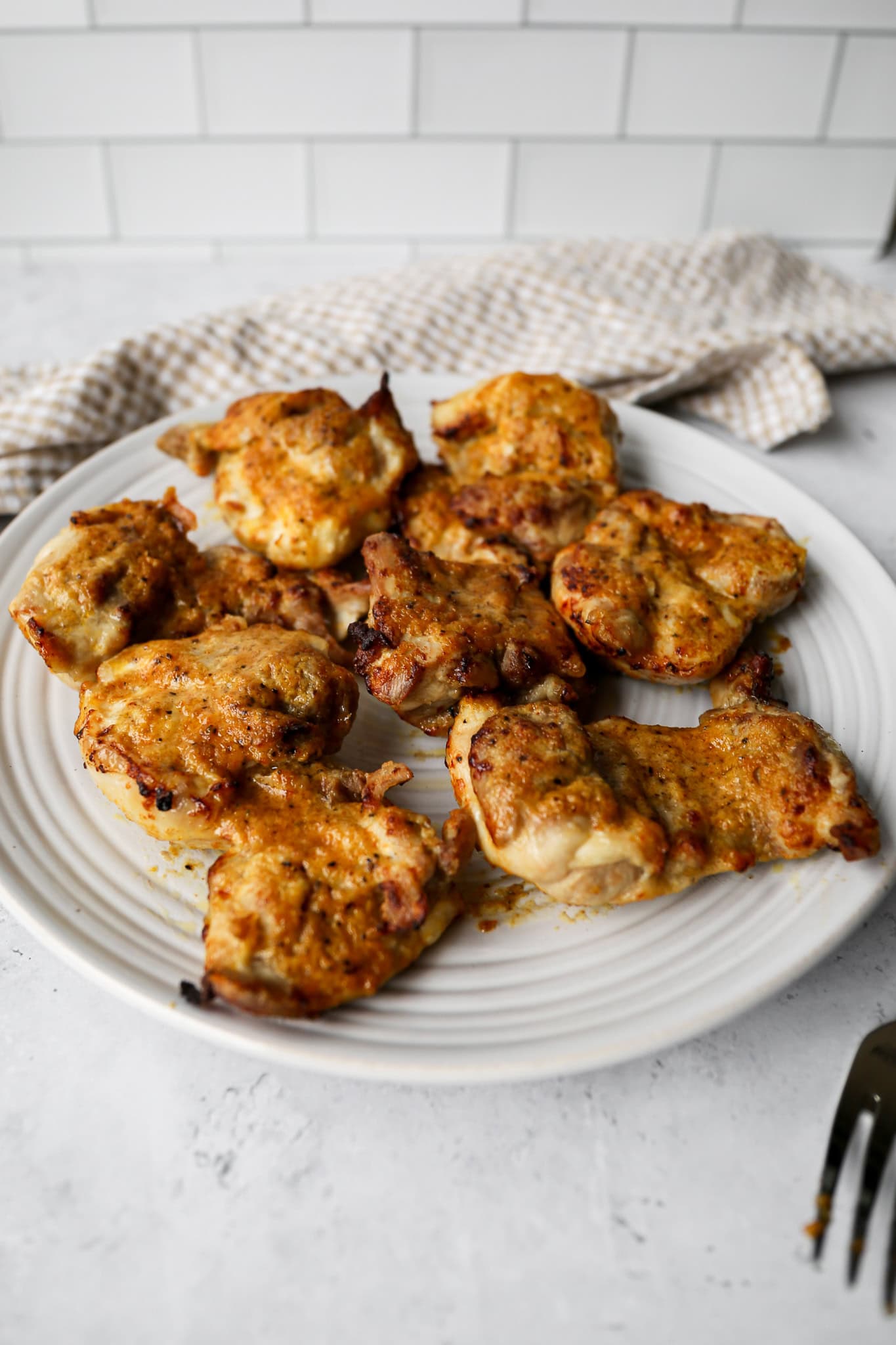air fryer teriyaki chicken thighs on a white plate next to a tan and white gingham kitchen towel