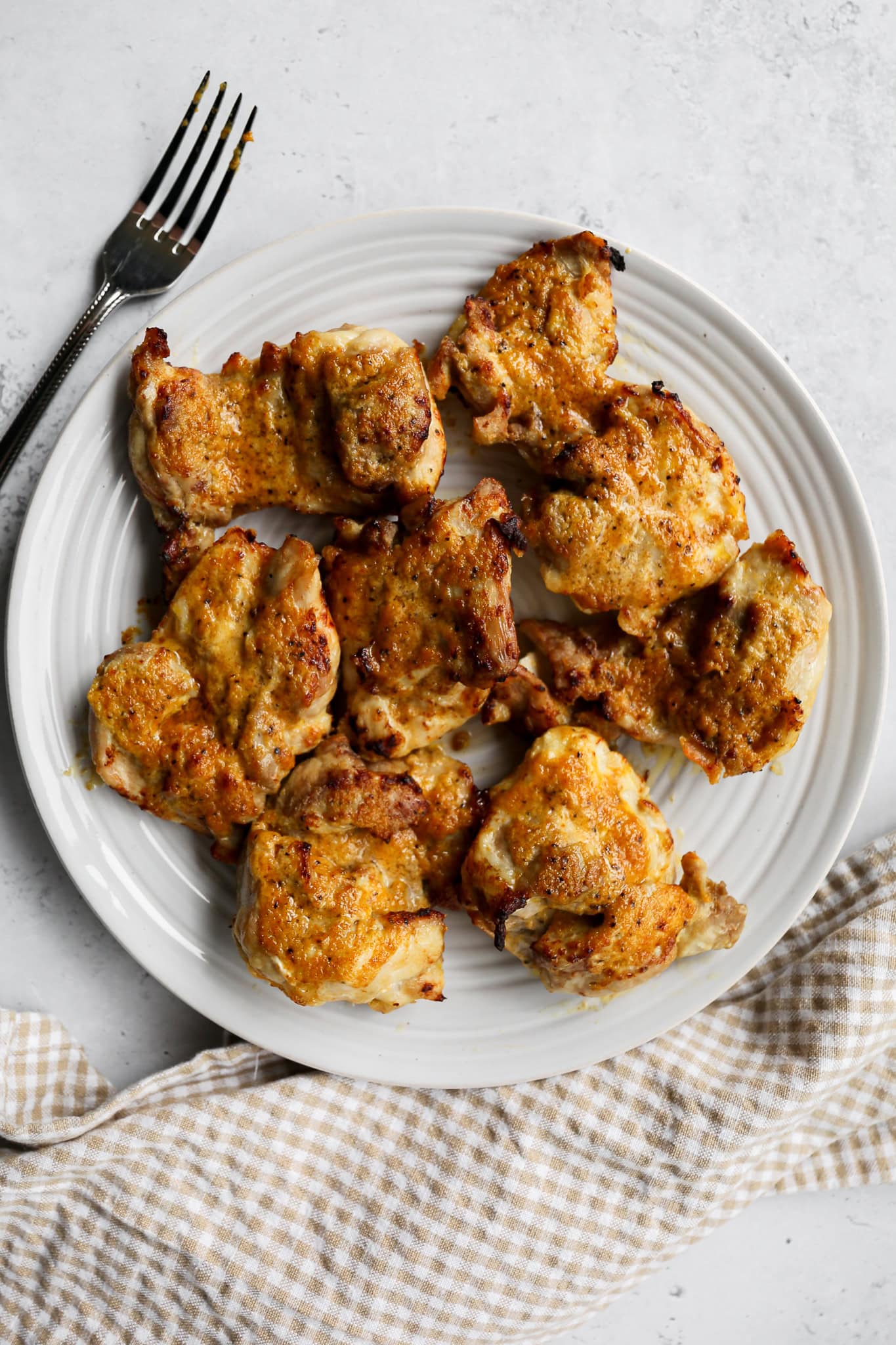 air fryer teriyaki chicken thighs on a white plate next to a tan and white gingham kitchen towel