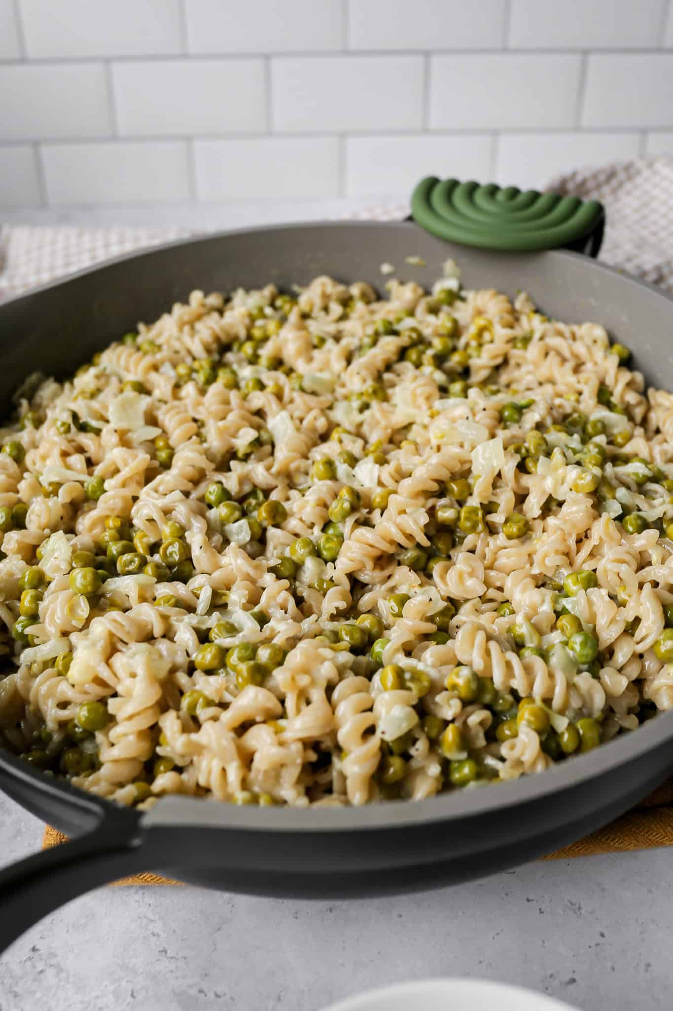 a pan of gluten free creamy peas and past next to a tan gingham kitchen towel