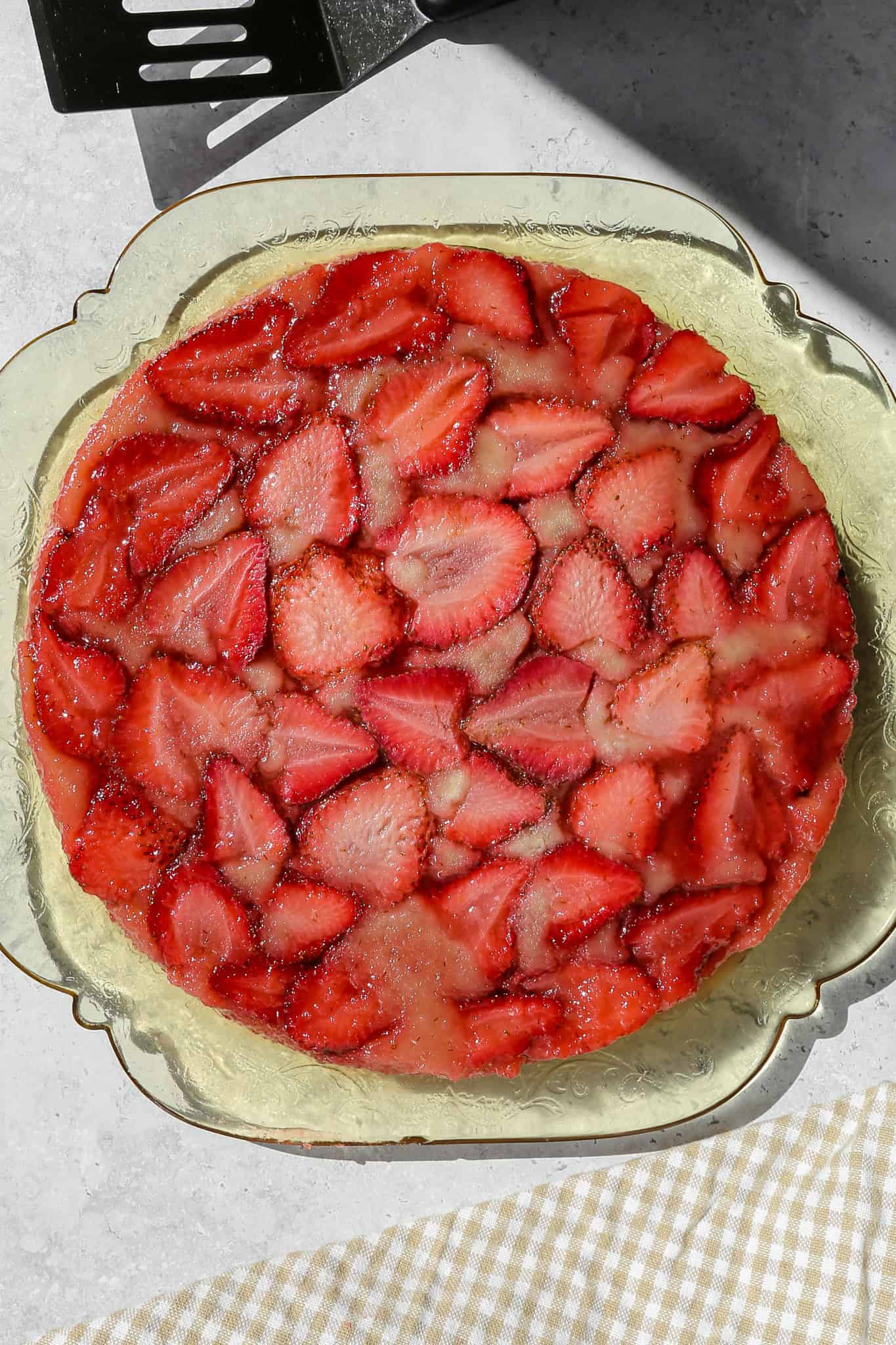gluten free strawberry upside down cake on a clear yellow antique platter next to a tan gingham kitchen towel