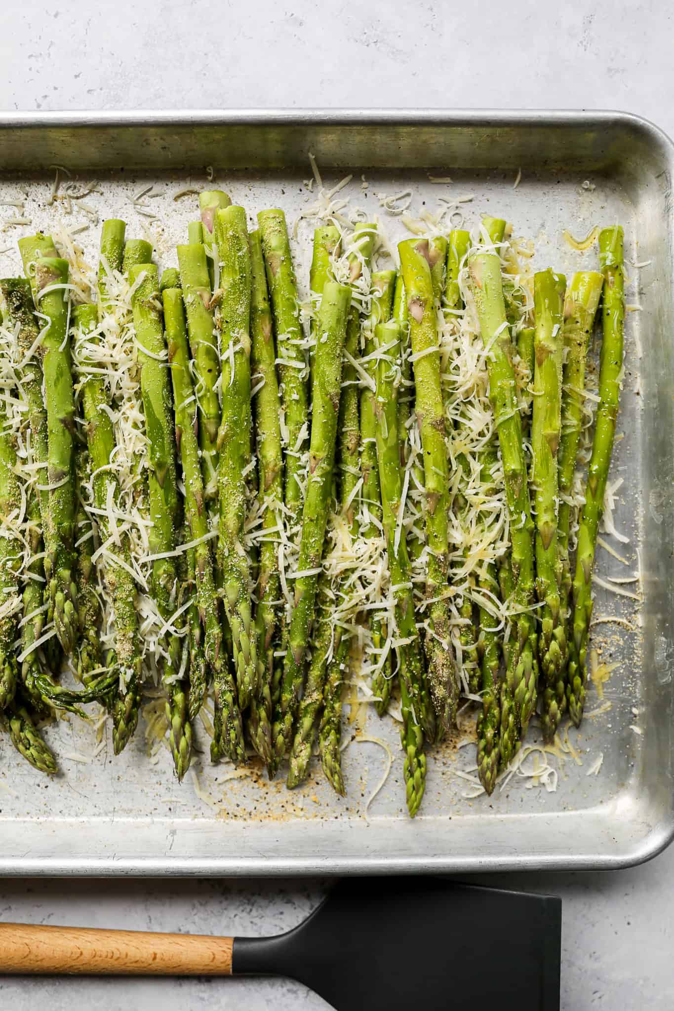asparagus on a silver baking pan sprinkled with parmesan cheese and a spice blend before going in the oven