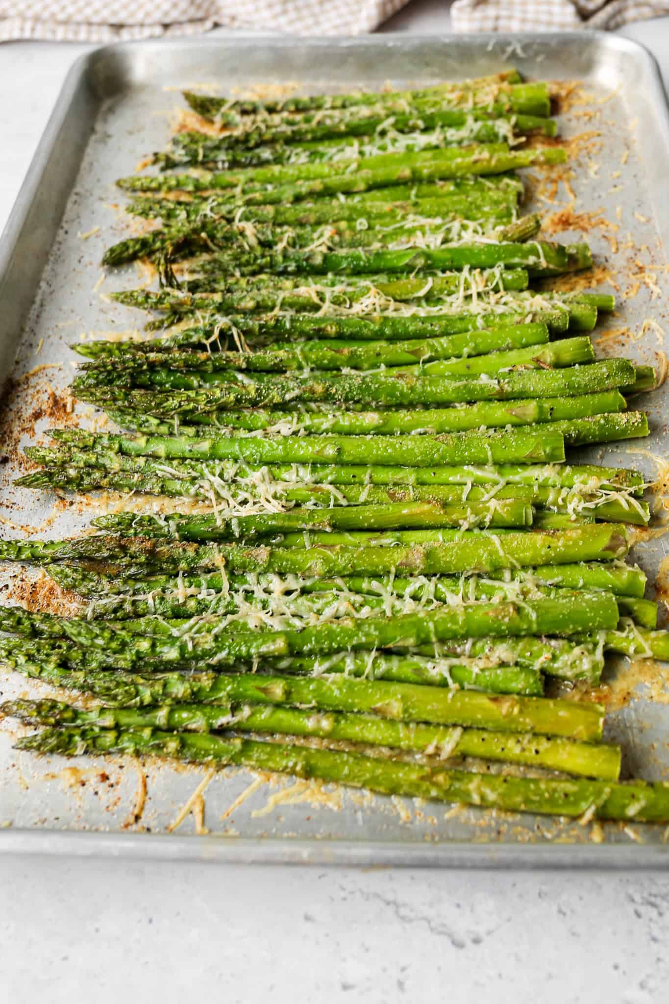 asparagus on a silver baking pan covered in melted parmesan cheese and a spice blend